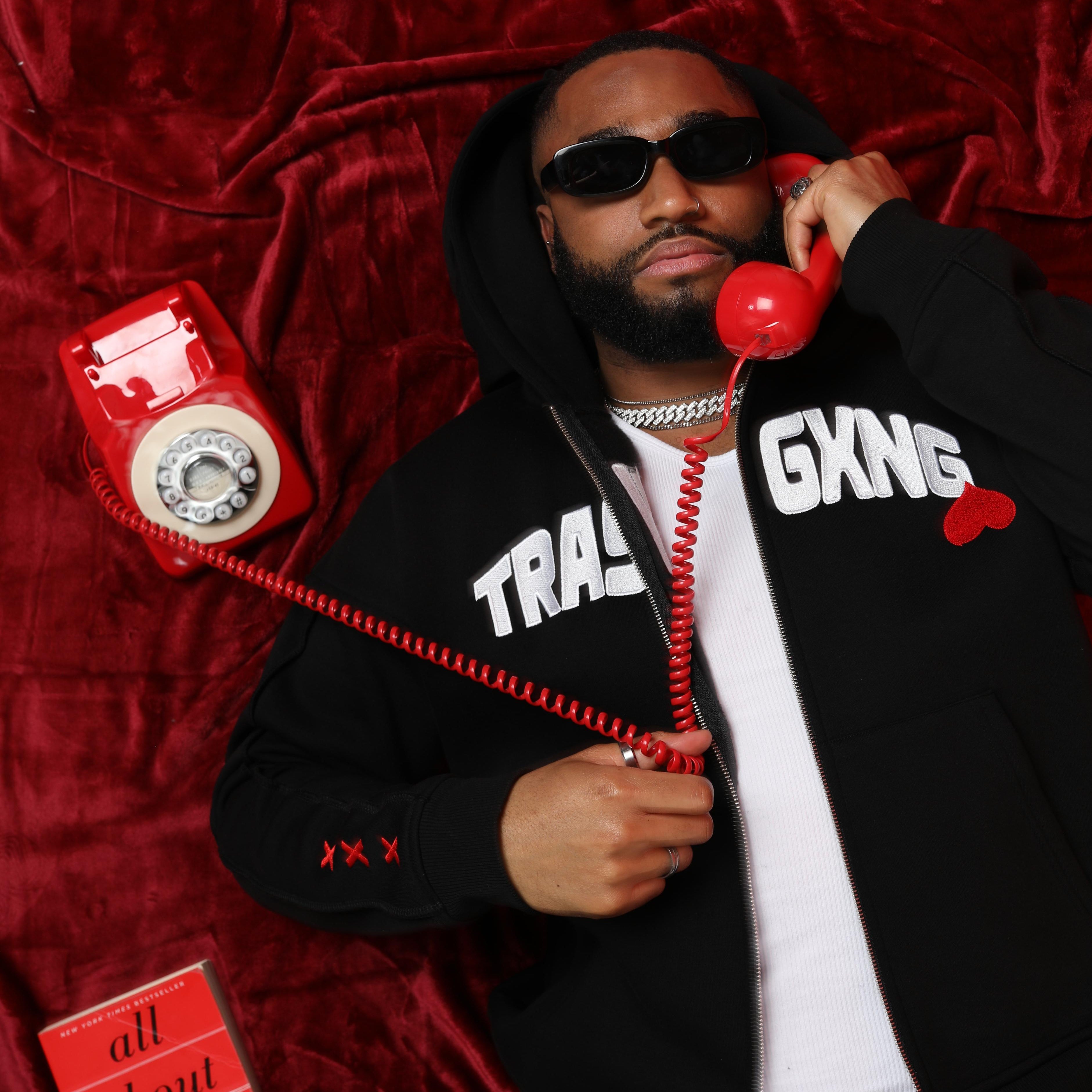 Lover boy laying down wearing OG Love black hoody, holding a red phone on a red background