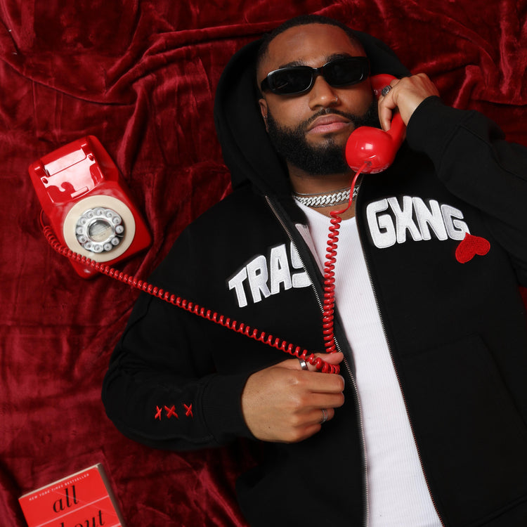 Lover boy laying down wearing OG Love black hoody, holding a red phone on a red background